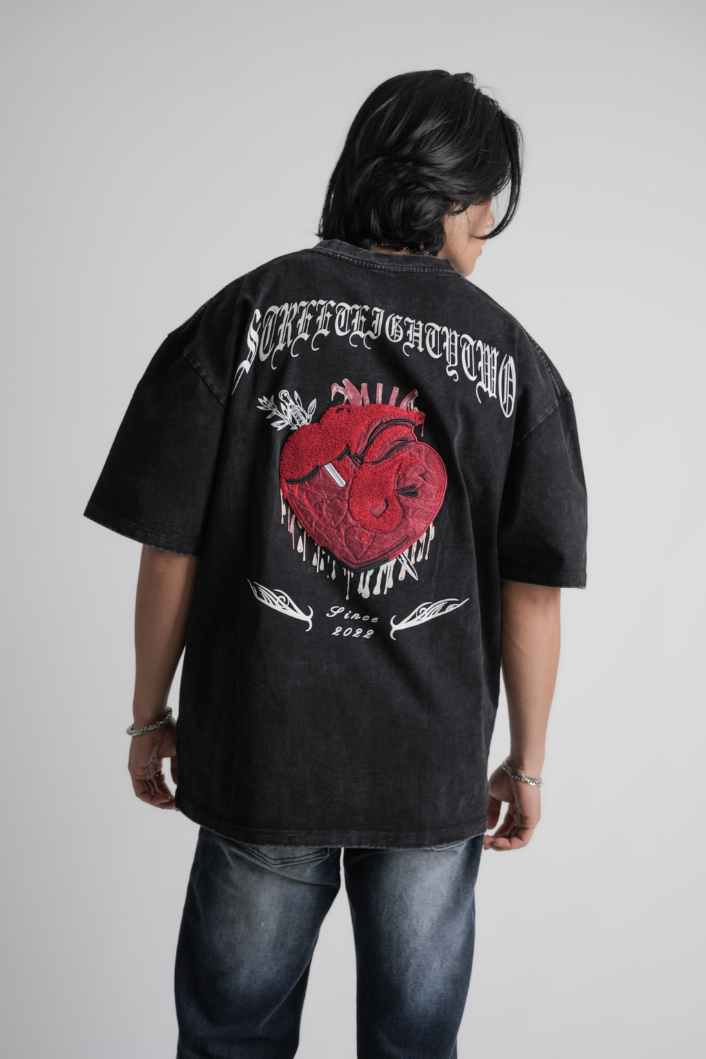 Person wearing a black oversize t-shirt with a red heart design and text on the back, standing against a plain background.
