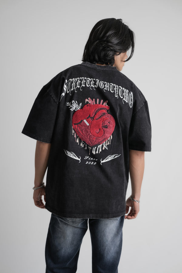 Person wearing a black oversize t-shirt with a red heart design and text on the back, standing against a plain background.