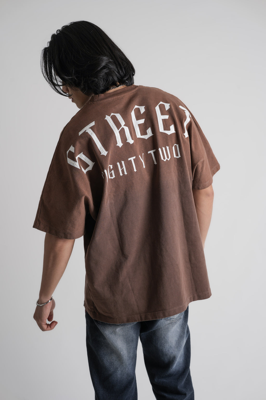 Person wearing a brown oversize t-shirt with text on the back against a plain background