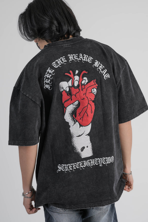 Person wearing a black oversize t-shirt with a graphic design on the back against a gray background