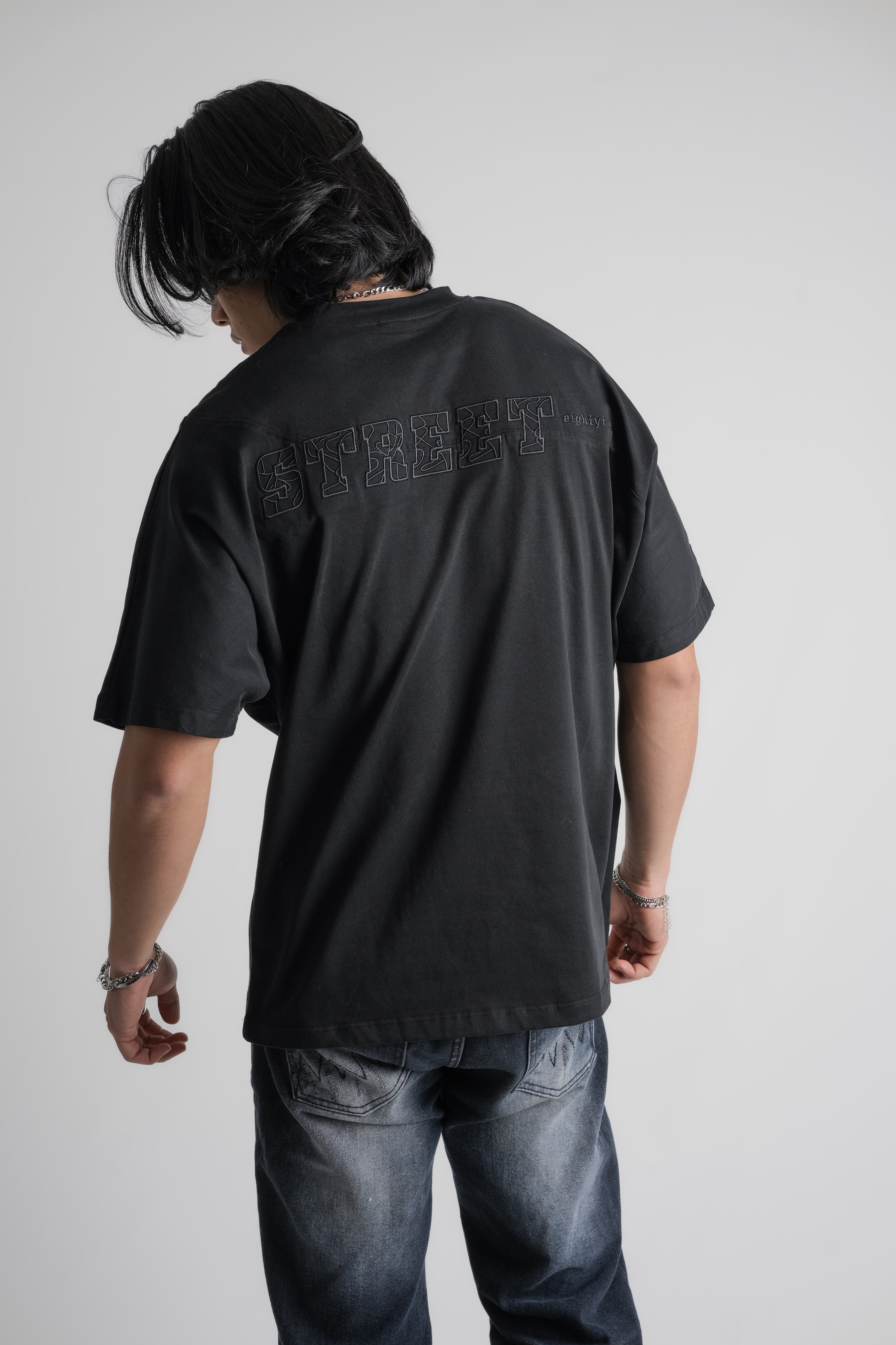Person wearing a black oversize  t-shirt with text on the back, standing against a plain background